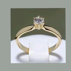 a yellow gold engagement ring with a single diamond in the center, on a white surface