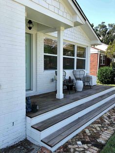 a white house with wooden steps leading up to the front door and patio furniture on the porch