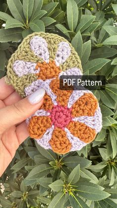 a hand holding a crocheted flower with leaves in the background