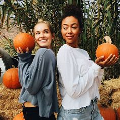 two women standing next to each other holding pumpkins