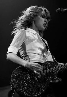 black and white photograph of a woman playing an electric guitar in front of a microphone