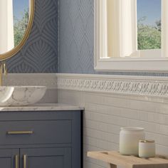 a bathroom with blue and white wallpaper, marble counter top sink and gold framed mirror