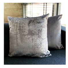 two silver pillows sitting on top of a blue couch in front of a brick wall