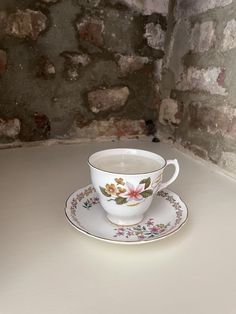 a tea cup and saucer sitting on a white counter top next to a brick wall