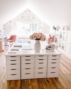 a room with white furniture and flowers in a vase on the top of the table