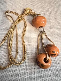 This is a fun piece of vintage VOGUE Jewelry. A large (25mm) mango-colored or pumpkin spice ceramic ball is the focal point with two 15mm hand painted balls dangling with gold plated foxtail chain. This is all suspended from a double gp foxtail chain measuring  22" long and knotted accents on each side. A real cute and creative piece of vintage VOGUE jewelry. It is in excellent vintage condition. Don't think it was ever worn! Retro Brown Necklace For Gift, Vintage Brown Necklace With Adjustable Chain, Vintage Brown Jewelry With Adjustable Chain, Retro Orange Necklace Gift, Vintage Handmade Orange Necklace, Vintage Long Orange Necklace, Vogue Jewelry, Necklace Ceramic, Ceramic Ball