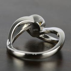 a silver ring with two hearts on it sitting on top of a wooden table in front of a black background