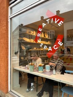 two people sitting at a table in front of a store window that says creative space