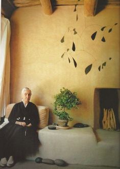 an old man sitting on a couch in front of a window with plants and other items