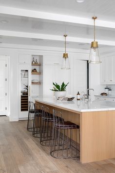 a large kitchen with white cabinets and wooden flooring, along with bar stools