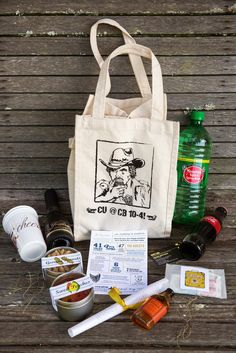 the contents of an outdoor picnic bag laid out on a wooden table with bottles and utensils