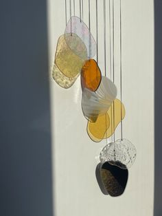 a group of different colored glass objects hanging from the side of a white wall with shadows on it