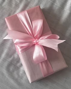 a pink present wrapped in satin ribbon on top of a bed