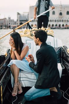 two people sitting in a gondola on the water with a man standing next to them