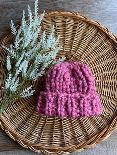 a pink crocheted hat sitting on top of a wicker basket next to a plant