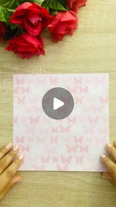 two hands holding up a piece of paper with pink butterflies on it and red roses in the background