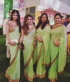 three women in green sari standing next to each other at a wedding ceremony with people looking on