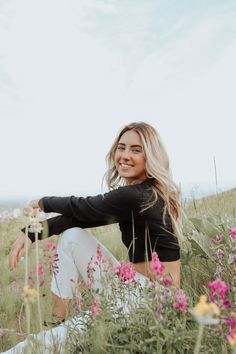 a woman sitting in the middle of a field with wildflowers on her knees