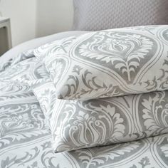 two pillows stacked on top of each other in front of a bed with gray and white sheets