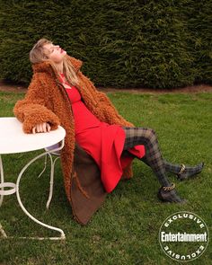 a woman sitting at a table in the grass with her eyes closed and she is wearing a red coat
