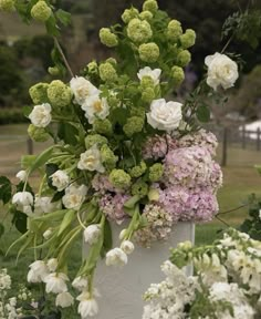 a white vase filled with lots of flowers on top of a lush green park field