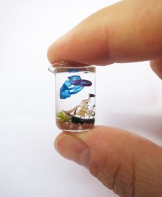 a hand holding a tiny glass jar filled with water and sea animals in the ocean