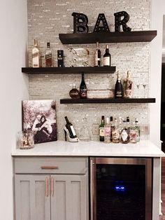 a wine bar with bottles and glasses on the counter top, along with shelves holding liquor