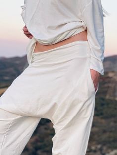 a woman in white pants standing on top of a hill