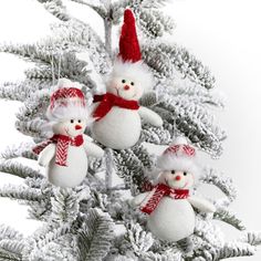 three snowmen are hanging from the branches of a christmas tree in red and white knitted hats