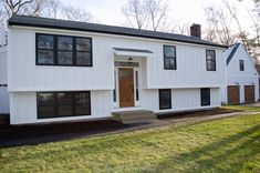 a white two story house with black shutters and wood doors on the front door