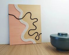 a painting on a wall next to a bowl and vase in a room with wood flooring