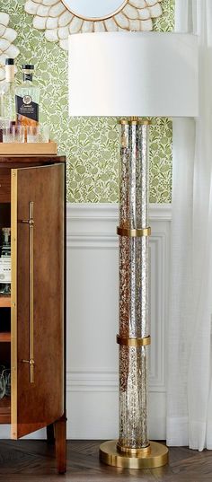 a tall lamp sitting on top of a wooden table next to a cabinet and mirror