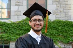 a man wearing glasses and a graduation cap standing in front of a building with ivy growing on it