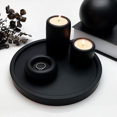 two candles sitting on top of a black tray next to a book and vase with flowers