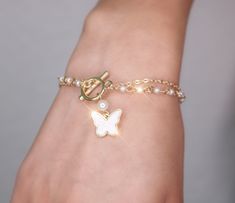 A stunning pearl chain butterfly bracelet that's perfect for any occasion. A piece that beautifully combines the classic allure of pearls with the delicate charm of a butterfly. Meaningful Symbolism: Butterflies are often associated with transformation and new beginnings, while pearls symbolize purity and wisdom. Wearing this bracelet serves as a beautiful reminder of personal growth and the beauty that comes with change. Gold plated alloy metal, acrylic mother of pearl and pearl beads Lead and Elegant Butterfly Bracelets For Gifts, Elegant Butterfly Bracelets For Gift, Elegant Adjustable Bracelets With Butterfly Charm, Elegant Butterfly Bracelets For Wedding, White Chain Bracelet With Pearl Drop As Gift, White Chain Bracelet With Pearl Drop For Gift, White Pearl Drop Chain Bracelet As Gift, White Butterfly Bracelet For Gift, Pearl Jewelry With Butterfly Charm As Gift