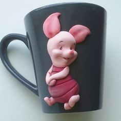 a ceramic piggy sitting on top of a black coffee cup with pink ears and tail