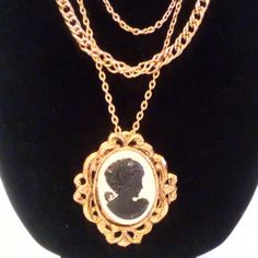 This Vintage Gold Tone Multi-Chain Cameo Necklace is an elegant statement piece, perfect for adding a touch of old-world charm to any outfit. The necklace features three distinct gold-tone chains of varying links and lengths, creating a beautiful layered effect. The shortest chain measures 20 inches, while the longest reaches 24 inches, offering a graceful drape. At the center of this stunning design is a large black and white cameo pendant, measuring 2 3/8 inches in length by 2 1/8 inches in width. The finely detailed cameo stands out against the vintage gold-tone setting, exuding timeless sophistication. The necklace fastens securely with a classic hinged clasp, ensuring both style and practicality. Victorian Gold Necklace With Figaro Chain, Vintage Delicate Chain Necklace, Vintage Delicate Chain Metal Necklace, Vintage Metal Layered Necklace For Gifts, Vintage Metal Layered Necklace For Gift, Vintage Multi-strand Layered Necklace For Gifts, Vintage Double Chain Metal Necklace, Vintage Antique Gold Jewelry With Gold Chain, Vintage Double Chain Necklace As Gift