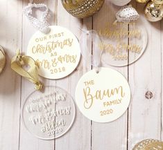 three personalized christmas ornaments on a white wooden table with gold and silver baubles