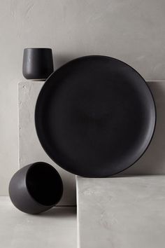 a black plate and two cups sitting on top of a white countertop next to each other