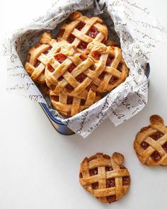 several small pies in a tin on a white table next to some cut out cookies