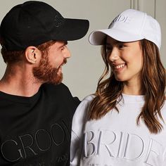 a man and woman standing next to each other in front of a white wall wearing matching hats