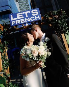 a bride and groom kissing in front of a sign that says let's french