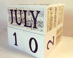 a wooden block with the word july written on it and music notes in black ink