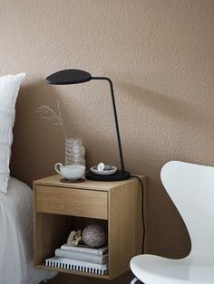 a nightstand with a lamp on top of it next to a white chair and bed