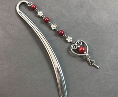 a red beaded necklace is hanging from a long silver hook with a heart and cross on it