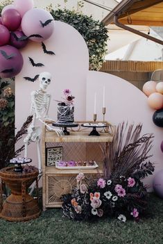 a table topped with cake and balloons next to a wall covered in halloween decorations on grass