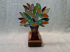 a glass vase with colorful leaves in it on a wooden stand against a white background