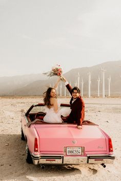 two people sitting in the back of a pink convertible car with windmills in the background