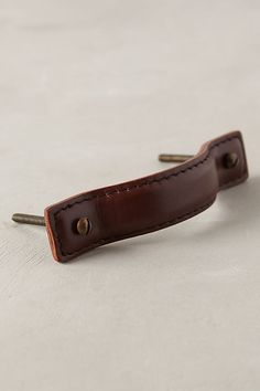 a brown leather tie clip with two screws in it's center on a white surface