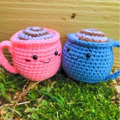 two crocheted coffee mugs sitting next to each other on the ground with grass